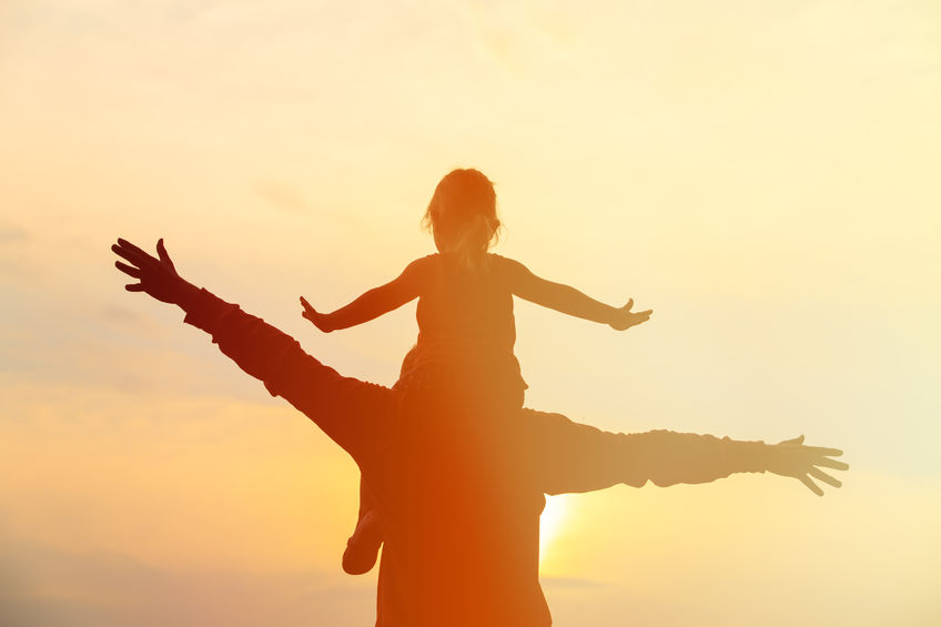 silhouette of father and little daughter on shoulders play at sunset sky